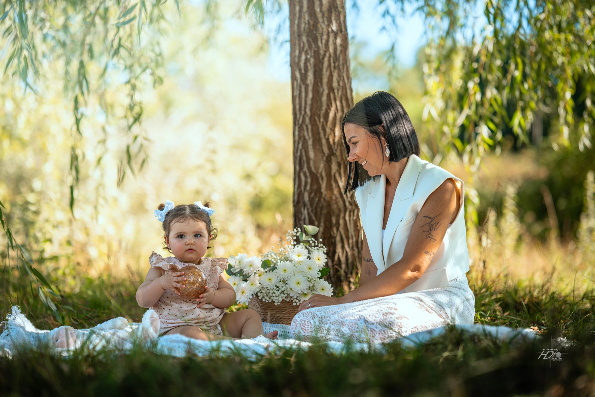 Une mère et sa fille assise sur l'herbe avec un bouquet de fleurs dans un panier en osier, prise à Bordeaux par leur photographe famille.