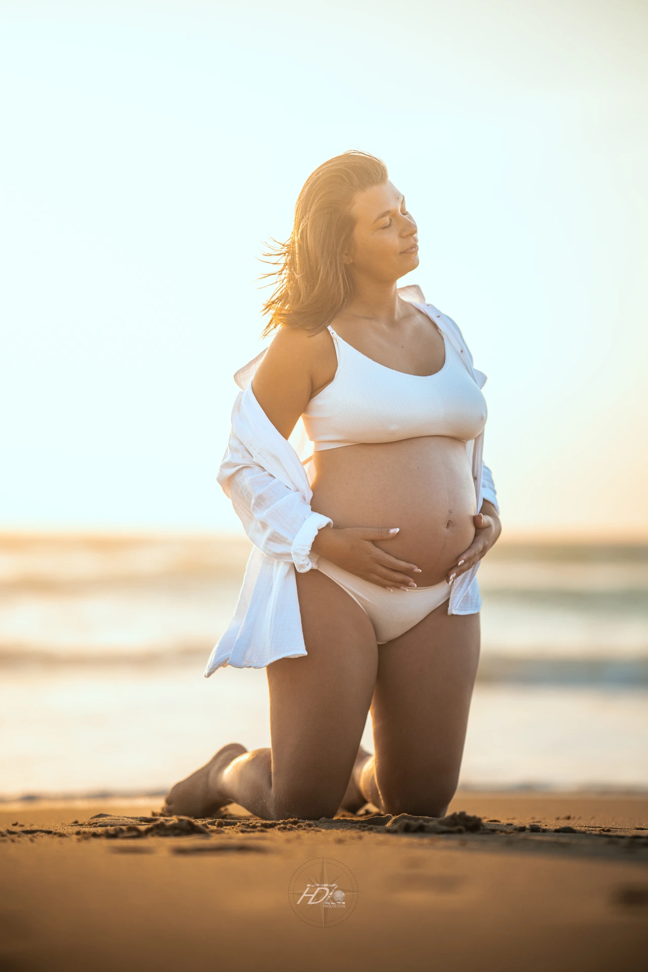 Un portrait d'une femme enceinte à la plage main sur son ventre lors d'un shooting grossesse à la plage à Arcachon au coucher de soleil