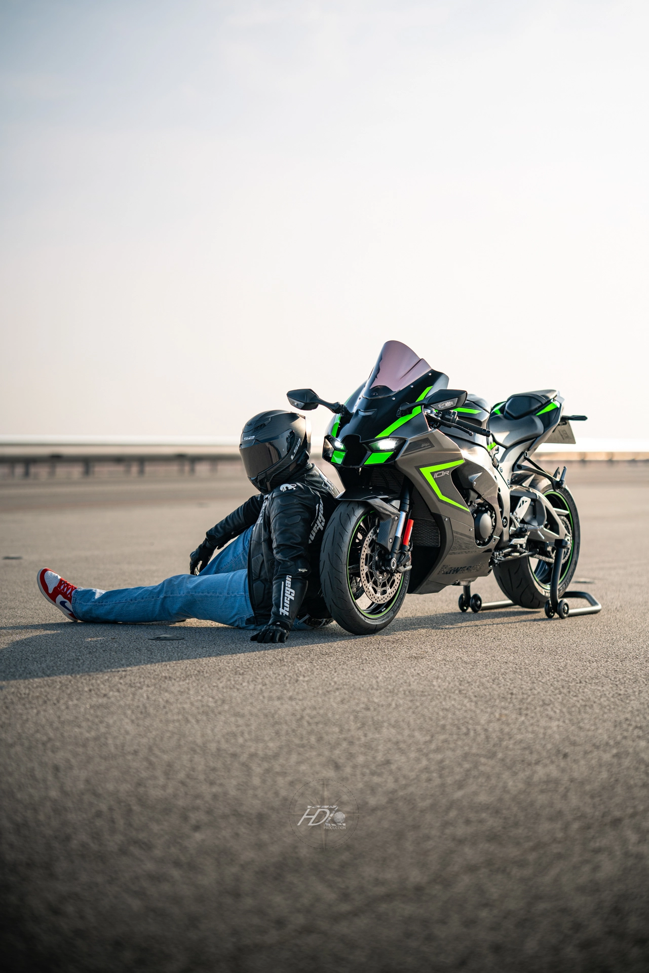 Un homme assis par terre et sa moto à côté regardent au loin.