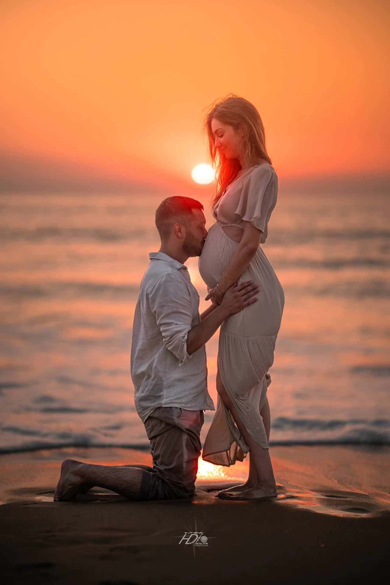 Le futur papa embrassant le ventre de maman lors d'une séance photo à la plage à côté de Bordeaux avec un coucher de soleil