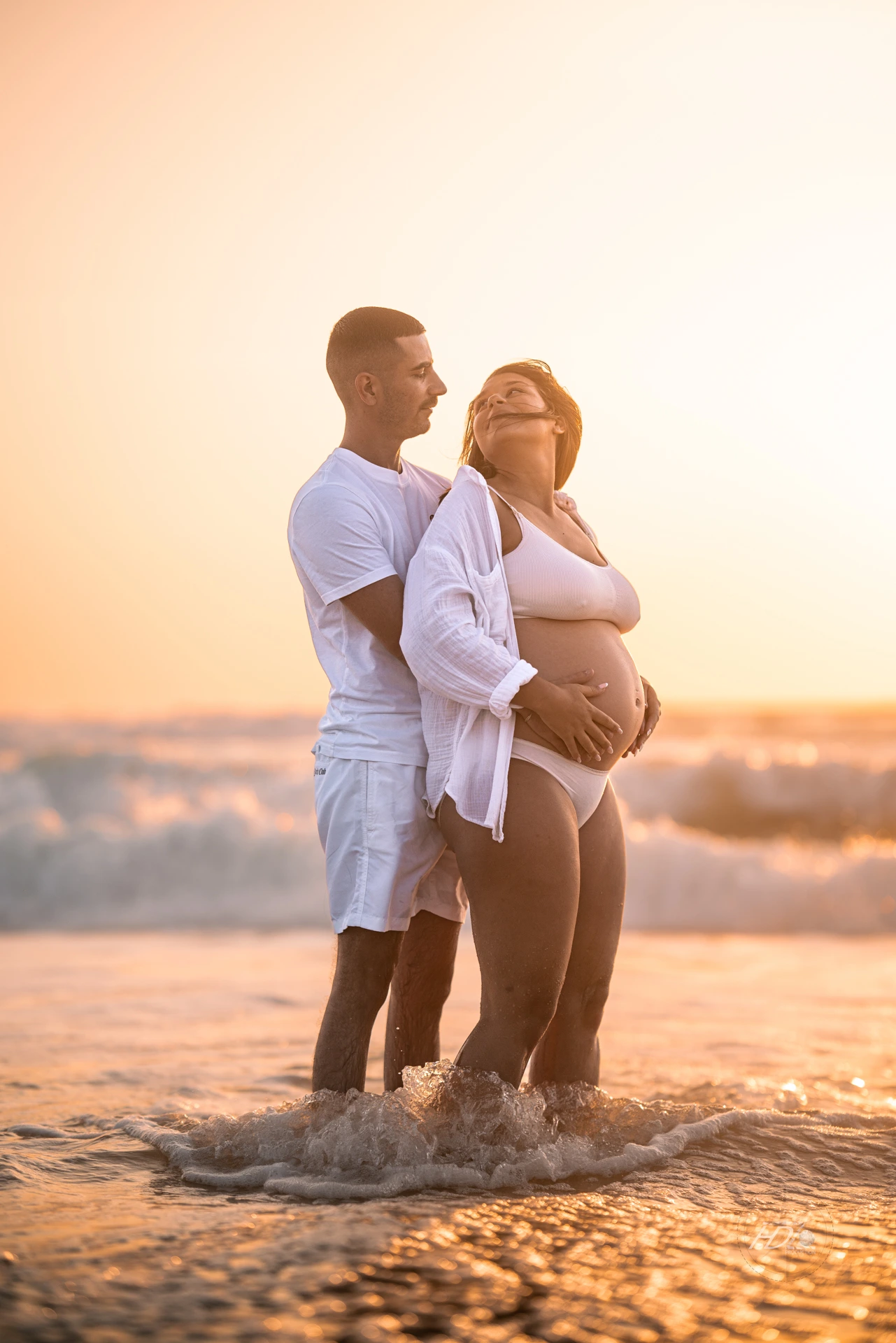 Un couple se regardant avec l'eau sur les pieds lors d'une séance photo grossesse à la plage avec la mer dans le fond à coté de Bordeaux