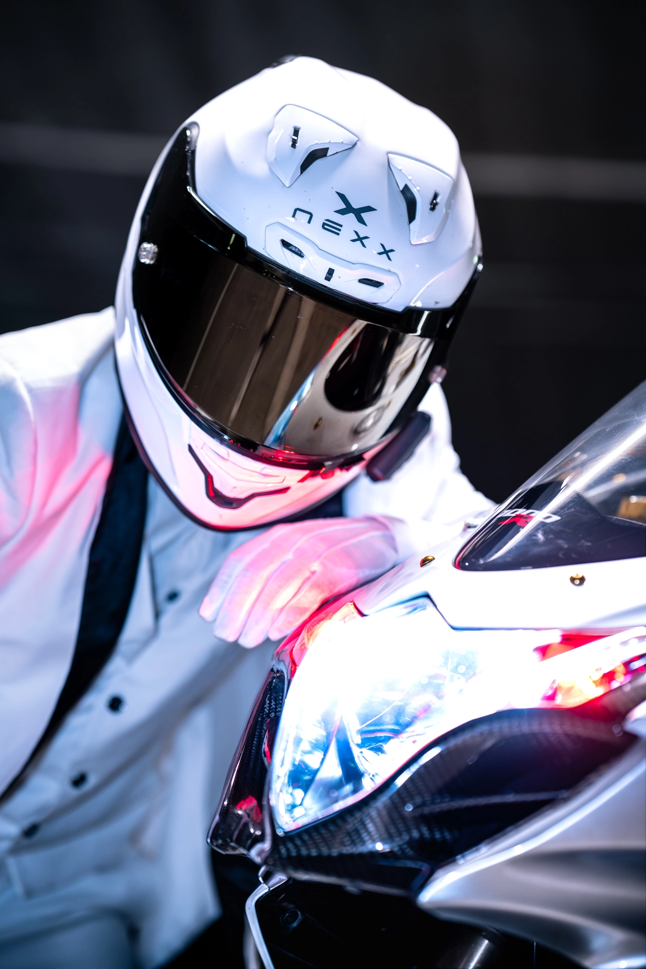 Un motard avec sa moto regarde vers le l'appareil photo.