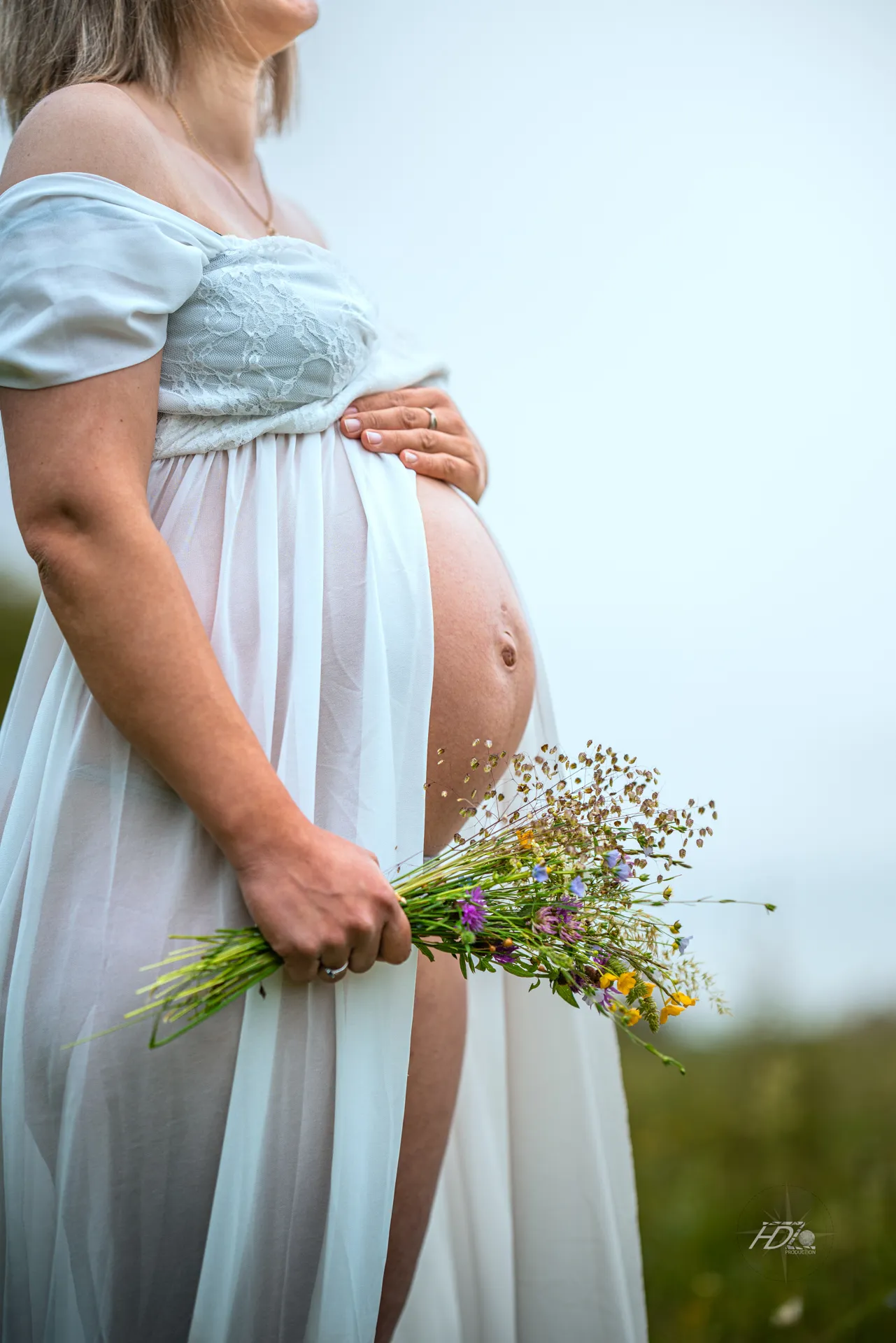 Une femme enceinte tenant un bouquet de fleurs à la main avec la main sur le ventre lors d'un shooting grossesse dans un champ
