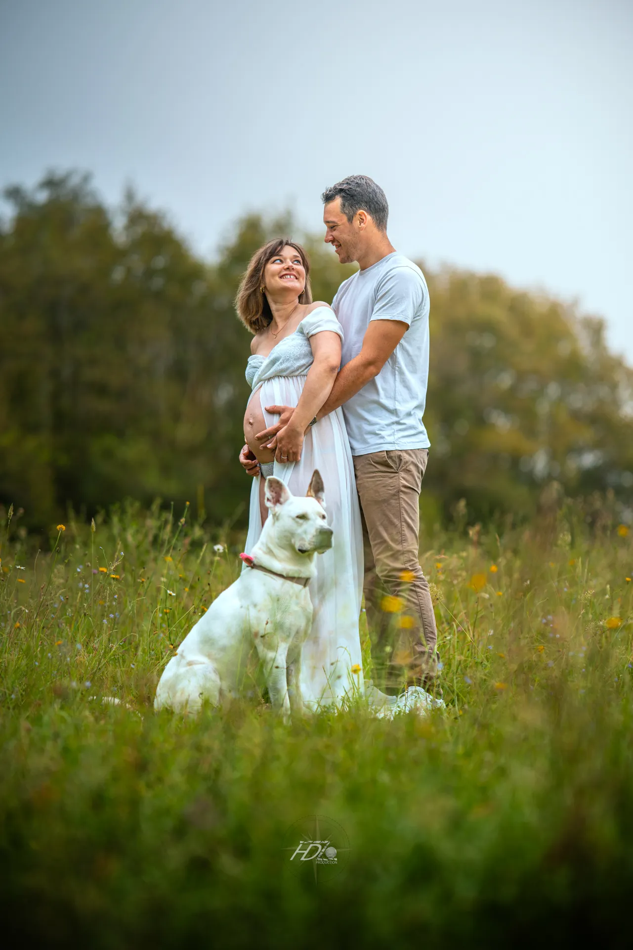 Un couple se regardant avec leur chien lors d'une séance photo grossesse dans un champ à côté de Bordeaux