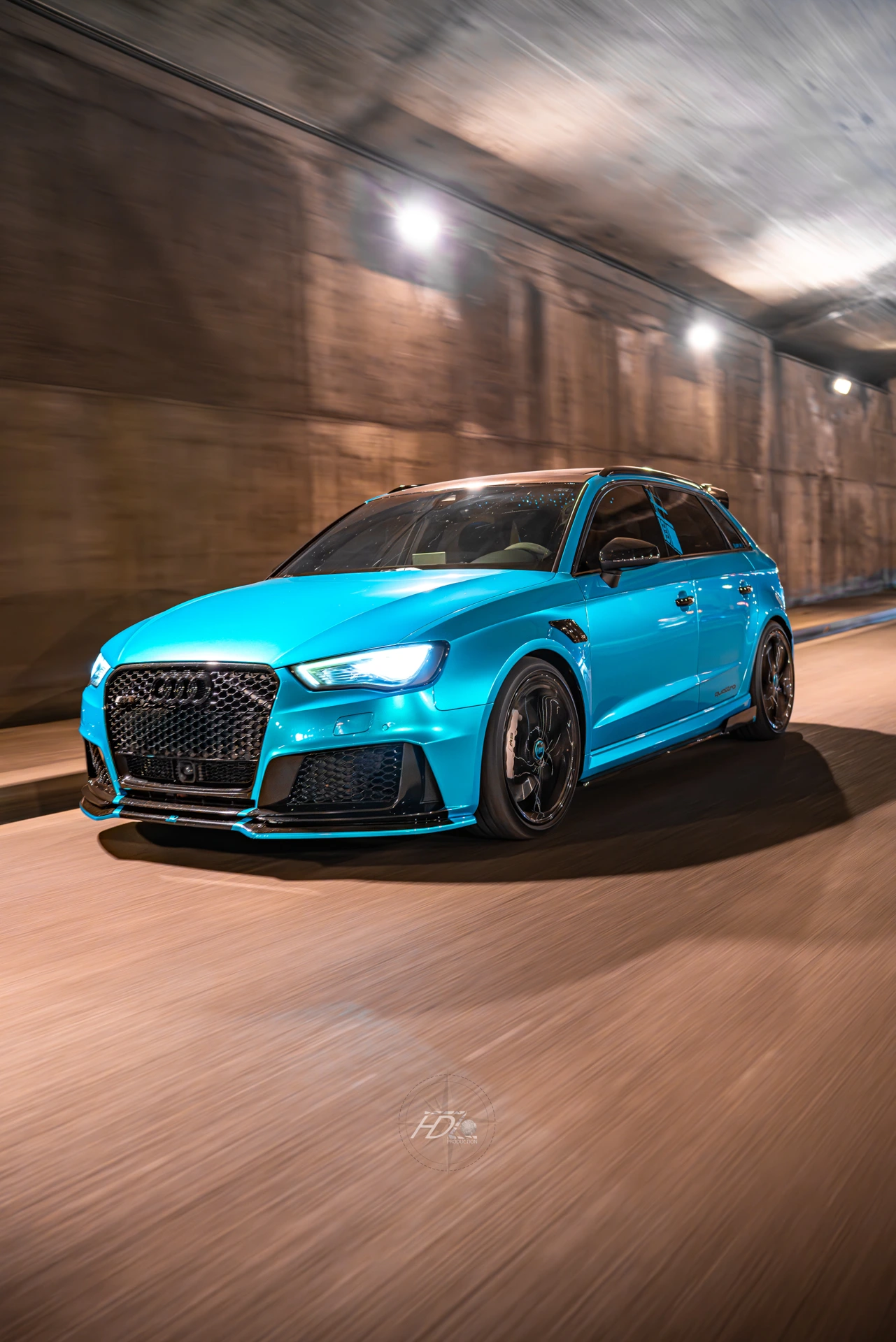 Une voiture bleu en train de rouler de nuit sous un pont.